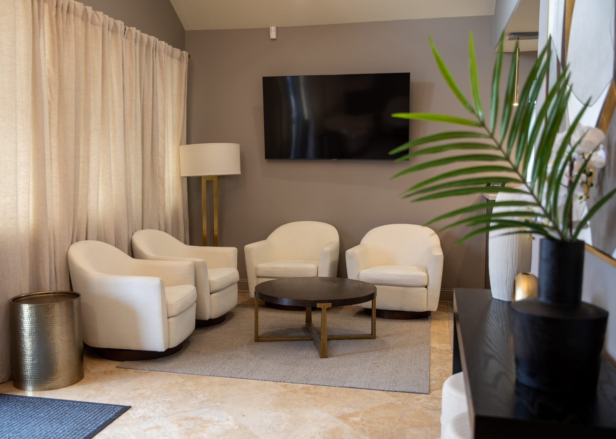 Modern waiting room with white armchairs, coffee table, lamp, TV, and decor.