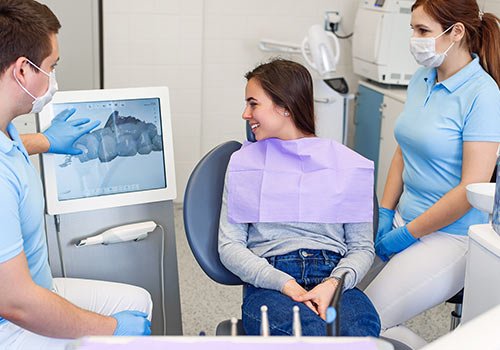 Smiling woman looking at computer monitor with two dental staff members