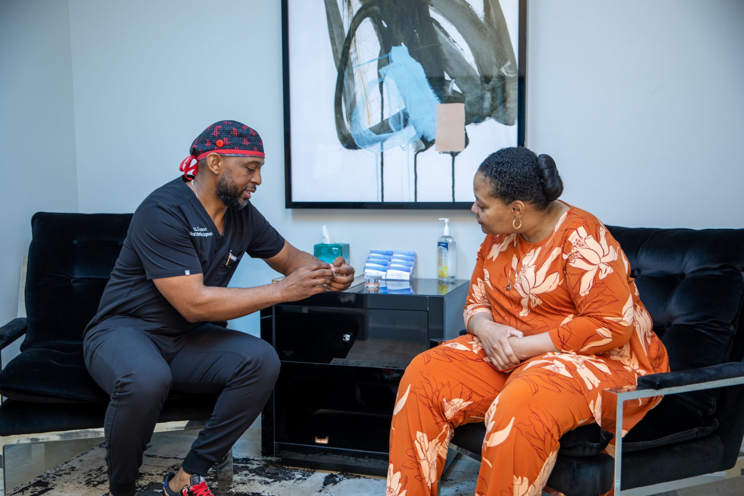A medical professional and a woman engaging in a consultation in a modern office, with artwork and supplies on a black side table in the background.