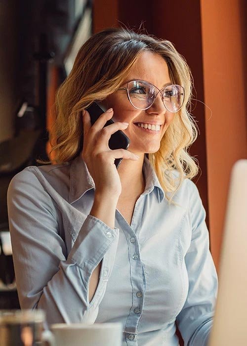 Blonde woman with glasses smiling while on her cell phone