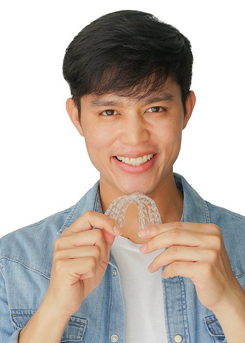 Asian man smiling, holding clear aligners